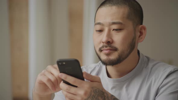 Young Adult Asian Man Browsing on His Smart Phone with Not Bad Facial Expression Indoors