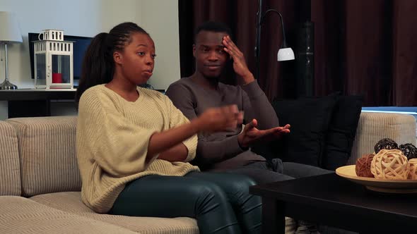 Young Black Unhappy Couple Watch Television in Living Room and They Are Angry