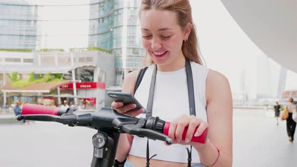 Young woman using smartphone scaning qr code unlocking kick scooter