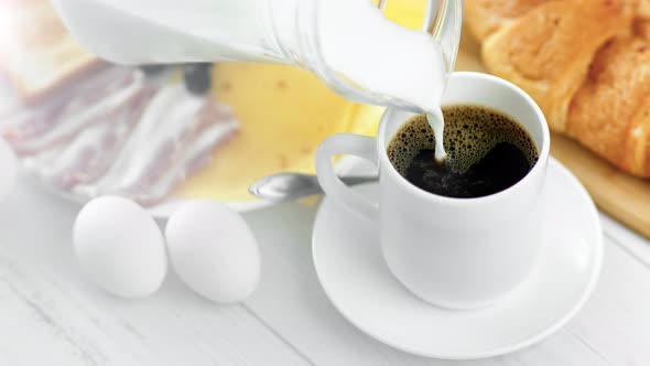 Pouring Milk From Jug Into Cup with Black Americano Coffee During Breakfast Closeup