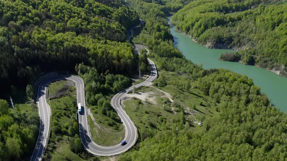 Aerial view of winding mountain road through the forest on lakeshore. Wide shot forward