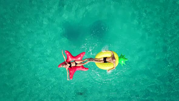 Aerial view of man and woman splashing each other on inflatable mattresses in sea.