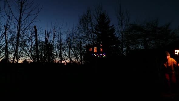 Illuminated treehouse at night, family at bonfire