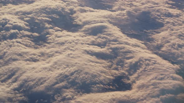 View Through Plane Window on Beautiful Sea of Fluffy Clouds in Sunset Light