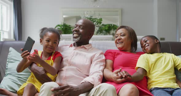 Happy african american grandparents and grandchildren sitting on sofa, taking selfie