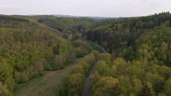 drone flight over green hills and meadows with a road in the valley past a huge farm