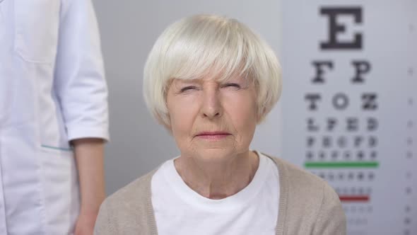Optician Comforting Elderly Woman Squeezing Eyes During Sight Examination, Care