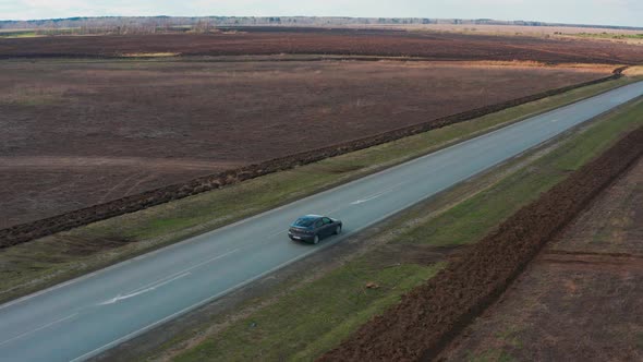 Cinematic Bird'seye View a Car Drives Over Rough Terrain on a Yellow Field