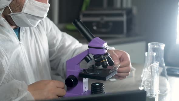 scientist man in laboratory in protective mask  looks into the microscope.