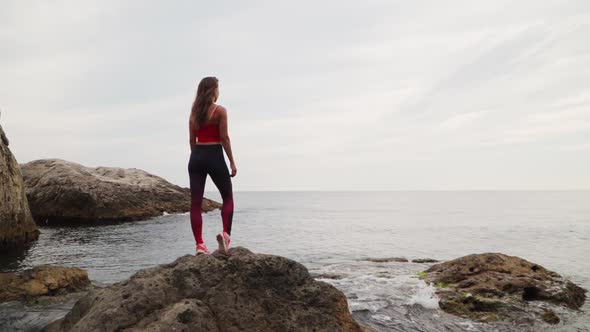 On a Stone in the Sea Is an Athletic Girl Traveler Sportswear