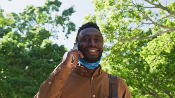 Smiling african american businessman with face mask talking on smartphone in street