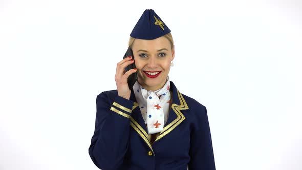 A Young Beautiful Stewardess Talks on a Smartphone While Looking at the Camera - White Screen Studio