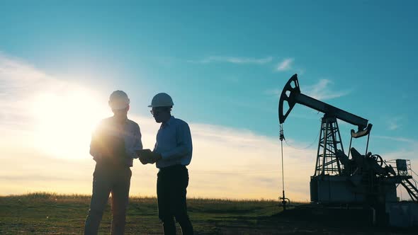 Two Oil Workers Talking in an Oil Field at Bright Sunset