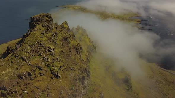 Aerial dolly in of verdant steep hills covered in clouds next to the sea, in Djúpivogur small town n