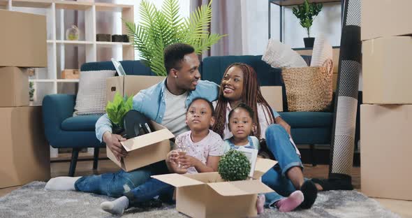 African American Couple with Two Small Daughters Sitting Together on the Floor Among Carton Boxes