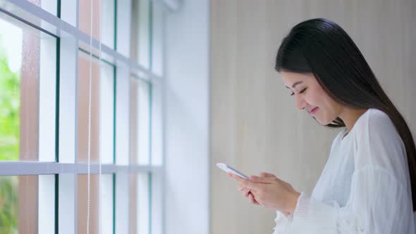 beautiful asian woman enjoy happiness hand use smartphone near window