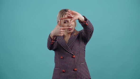 The Beautiful Young Blonde Puts Her Fingers in the Shape of a Picture and Looks Carefully Through It