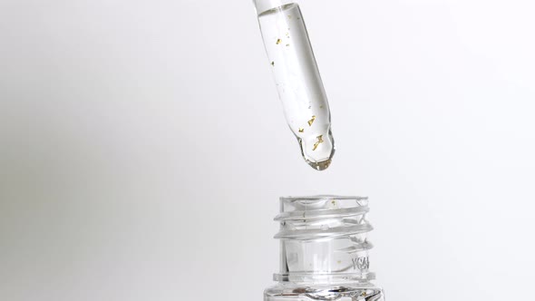 Serum with Gold Drops Falling From the Cosmetic Pipette on White Background