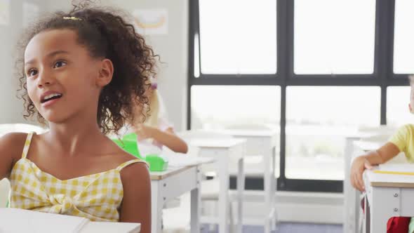 Video of happy diverse girls sitting at school desks and learning