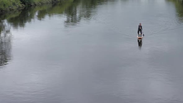 Caucasian man in sunglasses paddles paddleboard on calm rural river