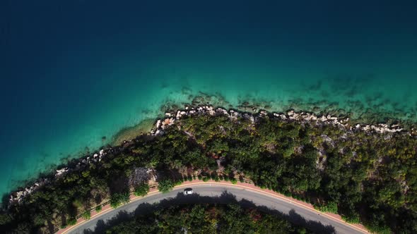 Aerial Drone Footage of Car Driving on the Serpentine Road Alone the Seashore with Transparent Water