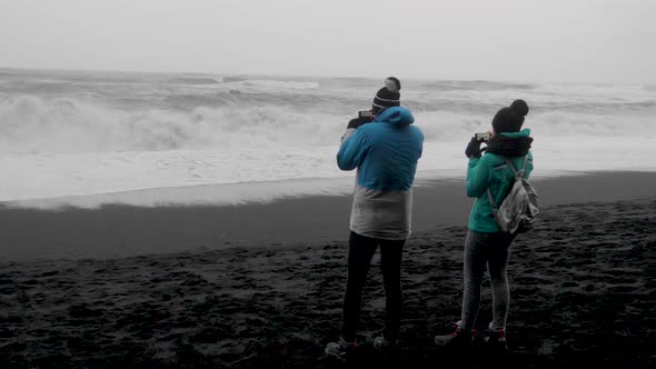 Static, shot, of people taking pics of the arctic sea, on a black sand beach, on a cloudy day, at Di