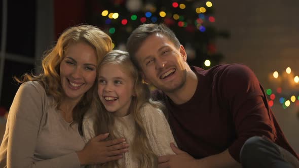 Young Family Hugging, Laughing and Looking to Camera, Christmas Lights Sparkling