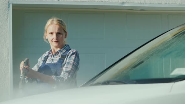 A Woman Washing My Car in the Backyard of Her House on the Background of the Doors To the Garage