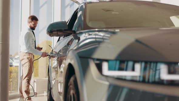 Handsome Business Man Holding Charging Cable for Electric Car