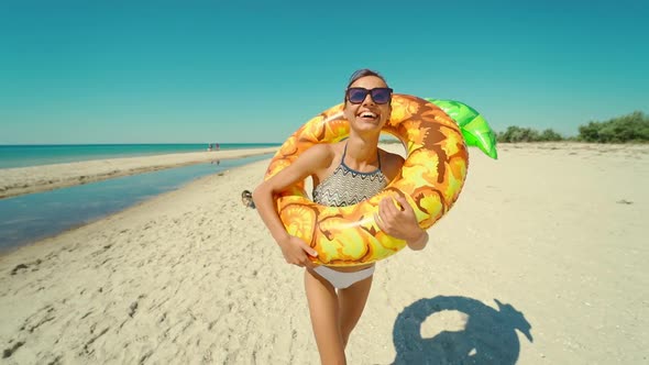 Cheerful Beautiful Young Millennial Woman Running on Empty Sunny Sandy Beach Holding Yellow