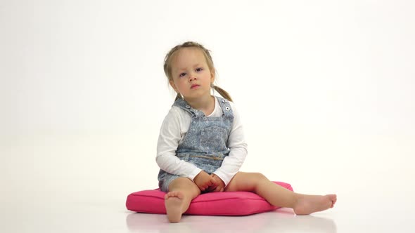 Little Girl Lies on the Floor and Raises Her Legs Up. White Background