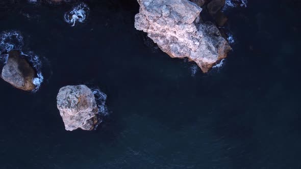 Top down aerial view of waves splash against rocky seashore, background. Flight over high cliffs of