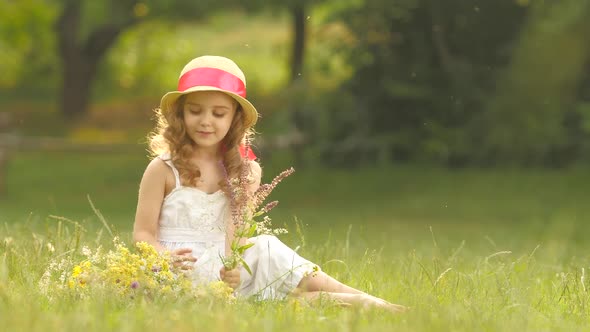 Little Girl Sits in a Clearing, Turns Over the Torn Wild Flowers and Makes a Bouquet From Them