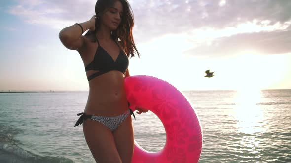 Beautiful Young Woman Walking with Colorful Inflatable Ring at Sea Coast During Sunset Slow Motion