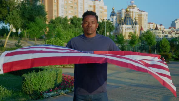 Portrait Afroamerican Man Holding an American Flag and Looks Camera in Summer