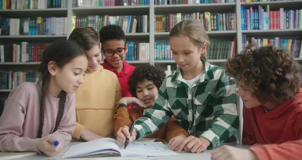 Blonde Girl Draws with Marker in Exercise Book in Library