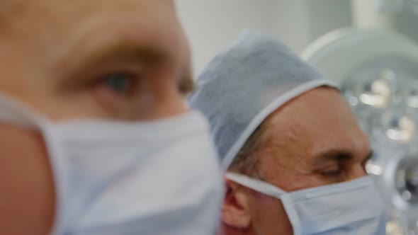 Two Caucasian male surgeons working together in a hospital operating theatre, wearing face mask for