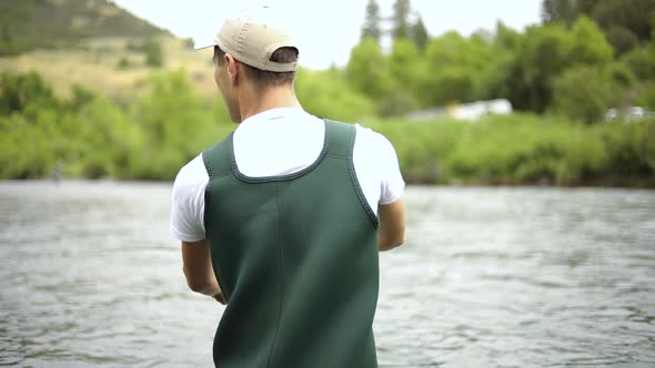 Slow Motion Shot of a Caucasian male fisherman casting his hook while Fly Fishing. He is standing in