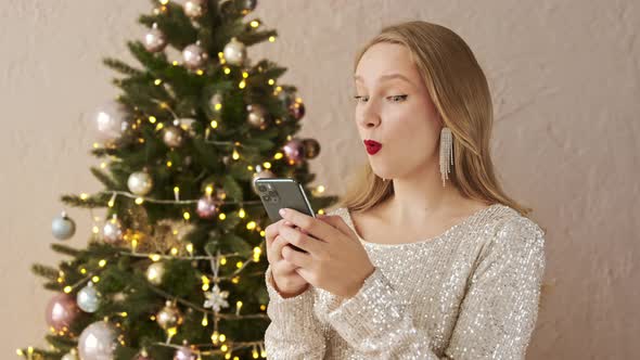 Amazed christmas woman using mobile phone, sees message with a good news or gossip and says wow.