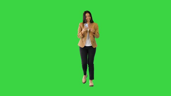 Young Indian Girl Walks and Smiles with Mobile Phone in Hands on a Green Screen Chroma Key