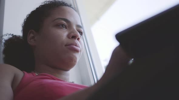 Cute Young African American Woman Sitting on the Window Sill Typing on Her Laptop. Happy Girl