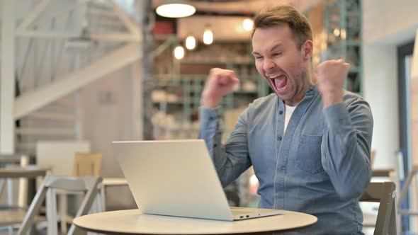 Casual Man Celebrating Success on Laptop in Cafe