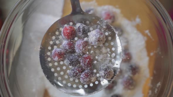 Slow motion close up view of sugar and cranberries sifting and being coated in clear glass bowl on w