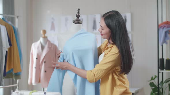 Smiling Asian Female Designer Wearing Fabric On A Mannequin While Designing Clothes In The Studio