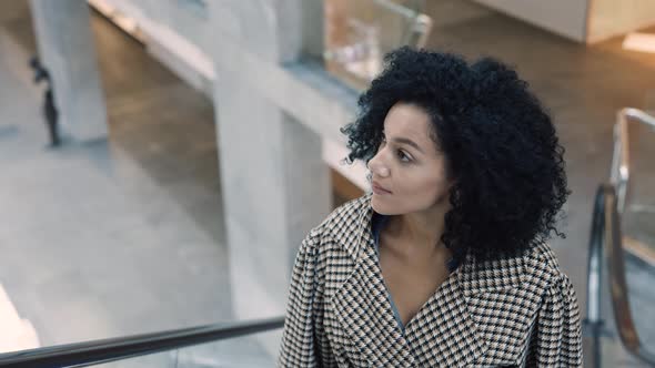 Stylish African American Woman in a Stylish Coat Climbs the Escalator in the Mall