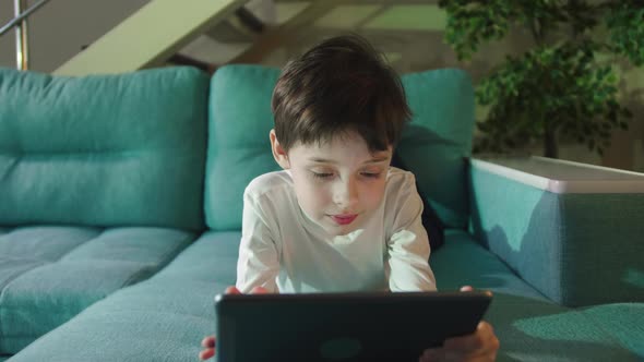 Adorable Kid Boy Using Digital Tablet Watching Cartoons Lying on Bed at Home.