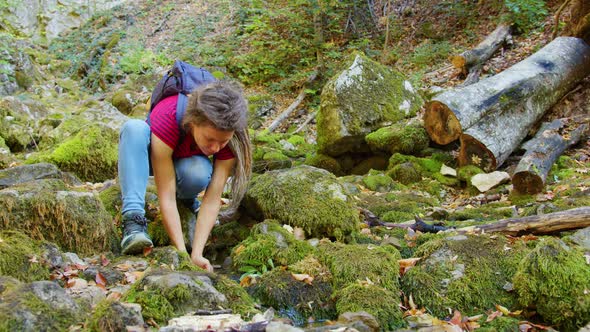 Young Woman Quenches Thirst Near Forest Brook