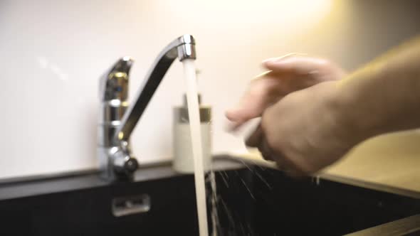 Long shot of male hands being thoroughly cleaned with soap by faucet
