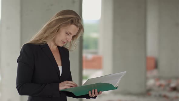 Female Architect Studying Drafts While Visiting Large Construction Site alt