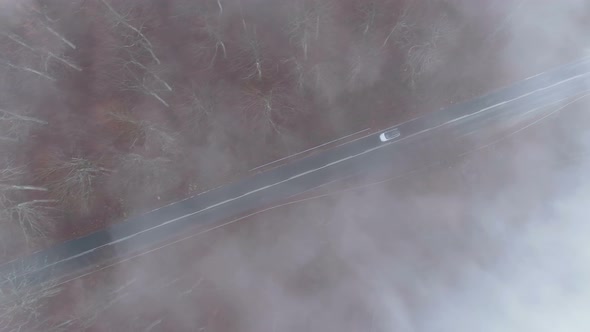 Drone Follows White Car Driving Slowly Through Dense Fog at Mountain Road